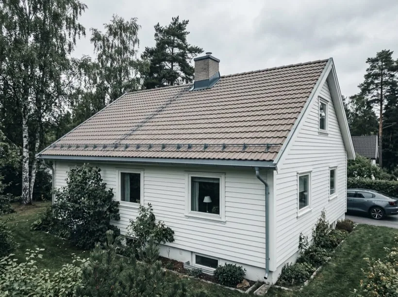 Illustrasjon av en hvit villa med et stort tak omgitt av bjørk og furutrær
