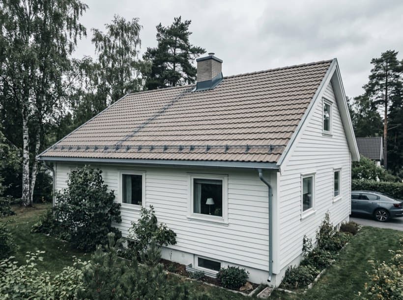 Illustrasjon av en hvit villa med et stort tak omgitt av bjørk og furutrær